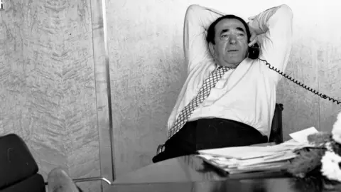 Getty Images Robert Maxwell leans back in his chair as he talks on an office phone with his feet resting on another chair