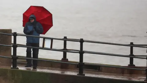 Reuters A man holding an umbrella by the coast in blustery conditions