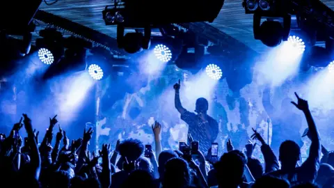 Ben Dance 6lack performs in front of a crowd on a brighty light lit stage