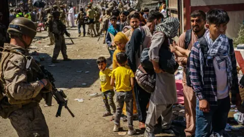 Getty Images Soldiers watch over Afghan refugees waiting in line to be processed for an exit flight out of Kabul