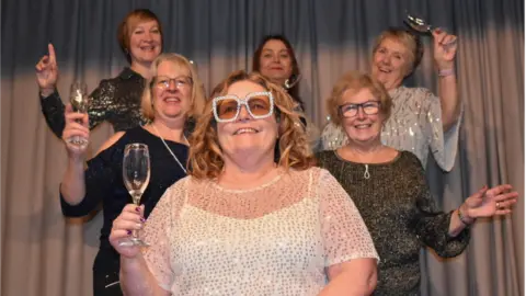 Kate James Kate James with members of the Bleadon Women's Institute. They are smiling and laughing and toasting the camera with wine glasses