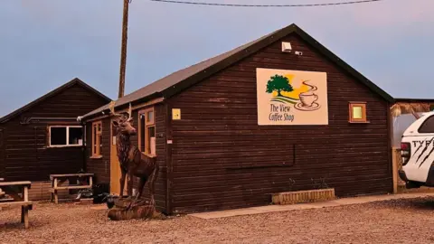 The View Coffee Shop Two wooden buildings with pitched roofs. The nearest building has a large white sign on the side which reads the View Coffee Shop. The furthest says Pavilion to Hire