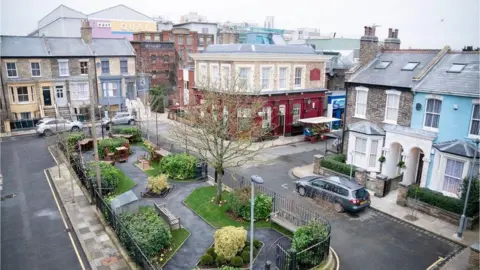 An aerial image showing the set of Albert Square in EastEnders. There is a small central garden surrounded by black railings, and the Queen Victoria pub is straight opposite. Notable character's homes surround the square.