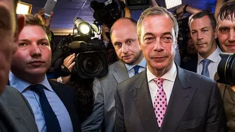 Nigel Farage arrives at the Leave.EU campaign's referendum party in 2016. To his far-right is George Cottrell wearing a light blue shirt and navy tie.