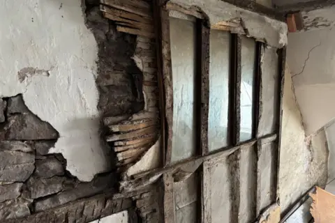 A wall of the secret chapel. A stone wall has patches of white plaster on it, a layer of horizontal wooden beams sits on top of it, with larger panelling on the right hand side.