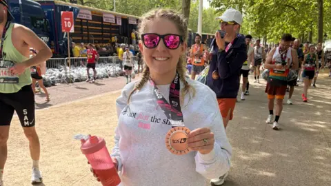 Gabriella smiling and holding up her finisher's medal.
