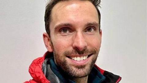Josh MacAlister, who is smiling and had a dark-coloured beard and hair, in his red mountain rescue jacket