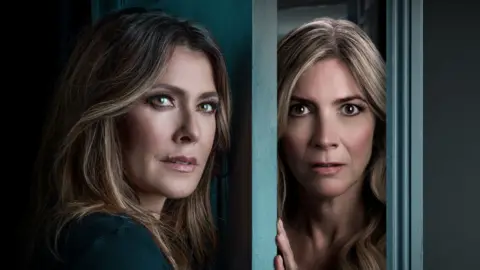 Single White Female Kym Marsh is staring off camera and is standing in front of a door, which is slight ajar, in a promotional shot for Single White Female. Her co-star Lisa Faulkner is standing behind the door and is staring directly at the camera.