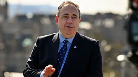Getty Images Alex Salmond, with thinning dark hair, speaks with a city backdrop behind him. He is wearing a dark suit and tie with a blue shirt. 