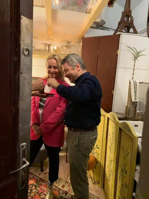 Katie Razzall/BBC Dr Gradel collecting gems being handed to him by another gem dealer in Paris
Hand  by door on left of image taking gems
Katie Razzall looking on