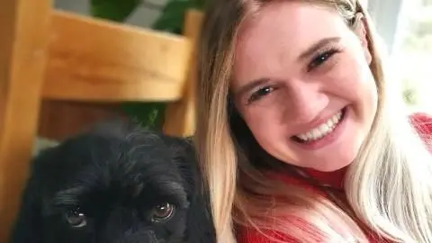 Newborough Family A women with long blonde hair, wearing a red top smiles for a selfie with a small black dog with big brown eyes.
