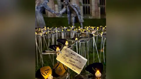 Clatterbridge Cancer Charity Steel flowers lit up in the garden of St Luke's Bombed Out Church with a close-up of a dedication which says for all of the amazing care from Clatterbridge.