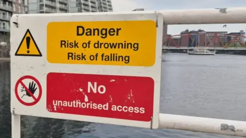 Yellow sign warning "Danger - Risk of drowning, risk of falling" above a red sign warning "no unauthroised access".