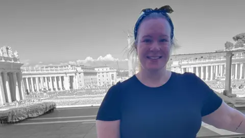 Family photo Georgie, wearing a black top and spotty hair ribbon, stands in front of a large historic building, smiling at the camera.