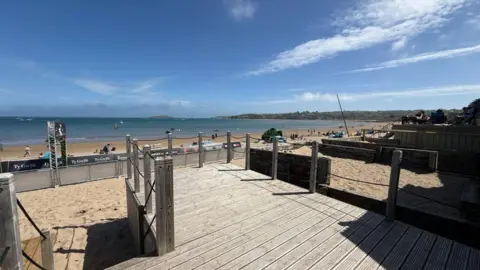 Elvins Estate Agents The view from the beach hut's wooden decking showing a long stretch of sand and sea on a sunny day.