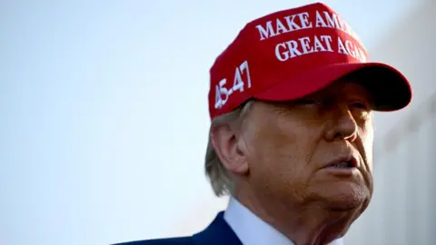 Donald Trump wearing a red baseball cap which reads 'Make America Great Again' and has the numbers 45 and 47 embroidered on the side, referring to his previous tenure as the 45th US president and his forthcoming term as the 47th