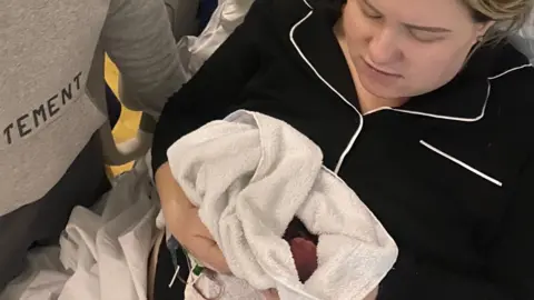Lewis Robinson A woman in black and white pyjamas holds a baby in a blanket.