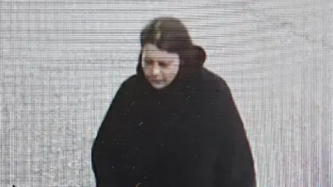 Police Scotland A grainy CCTV image of a woman with dark hair in a dark coat