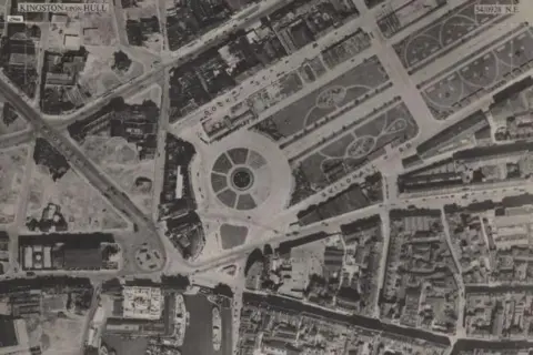 National Library of Scotland A black-and-white aerial view of a city centre. In the centre, a large formal park can be seen. Below it is a dock and to the right a square, which is surrounded by bomb sites, denoted by lighter-looking land. To the right, tightly-packed buildings can be seen.