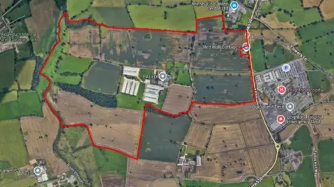 Google An aerial view of a rural area with a patch of it outline in red. There are labels, identifying some buildings and facilities nearby.