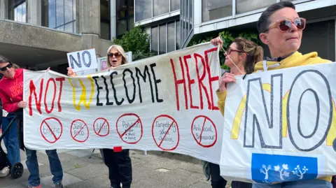 George Carden/BBC Residents holding signs outside hove town hall which say 'not welcome here'
