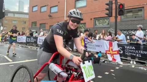 Supplied Tully Kearney, wearing a cycling helmet and shades, runs using her red-coloured three wheel frame 