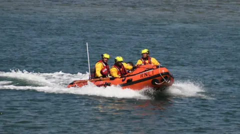Wells RNLI An orange RNLI lifeboat out at sea with crew dressed in yellow.