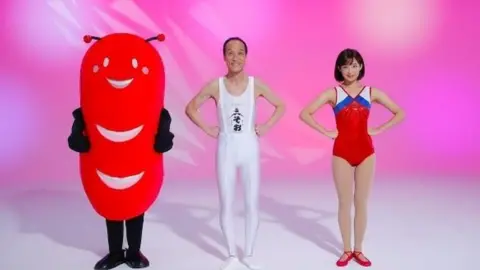Soo City Hideo Higashikokubaru stars with a gymnast (R) and an alien sausage mascot (L)