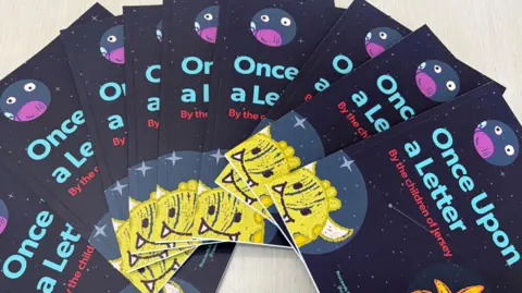 A pile of books fanned out over a table. The books are dark in color, with a little yellow monster in the corner and read the words 'Once upon a letter' a long the front.