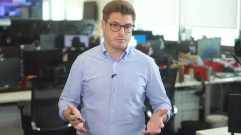 BBC journalist Nick Marsh has short brown hair and is wearing glasses and a blue shirt.