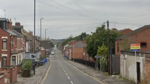Street going down a hill with houses either side and grey sky above
