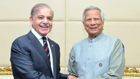 X/Shehbaz Sharif Dalam foto selebaran ini yang dirilis oleh Departemen Informasi Pers Pakistan (PID), Perdana Menteri Pakistan Shehbaz Sharif (L) berjabat tangan dengan pemimpin sementara Bangladesh Muhammad Yunus selama pertemuan bilateral di sela-sela KTT D-8 di Kairo pada 19, 2024. 