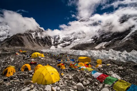 Getty Images GORAKSHEP, SOLU KHUMBU, NEPAL - 2019/09/15: Tents set up at Everest Base Camp on Khumbu glacier, Mt. Everest behind covered by monsoon clouds. (Photo by Frank Bienewald/LightRocket via Getty Images)