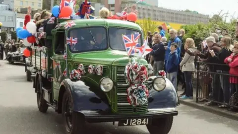 BBC Car passes crowds with people piled up in the back