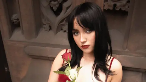 A woman with black hair in a red dress holding white and red roses