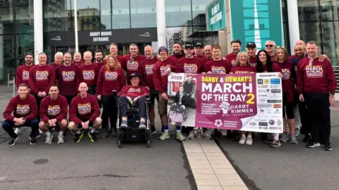 Darby Rimmer Redwood Events A group of people wearing March of the Day 2 jumpers and holding a banner are outside Wembley Stadium