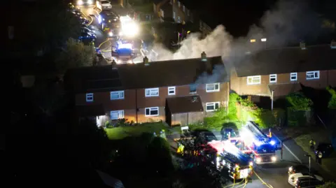 Smoke billows from the top window of a terraced house. 