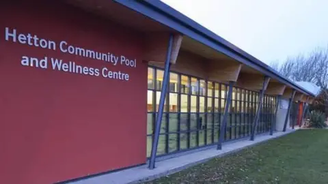 Google  A picture of the front of Hetton Community Pool, it is a long one story building with lots of glass panels through which you can just see the pool 