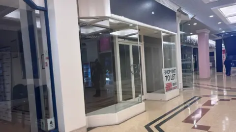 An empty shop unit, with a sign in the corner saying Shop Unit To Let