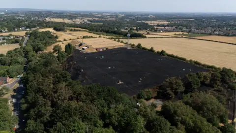 Jacob King/PA Wire An aerial shot of a large patch of a burned field after a large grassfire caused damage. A number of other fields are in the surrounding area, as well as dozens of green trees which were unaffected by the blaze.