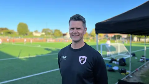 BBC Adam smiles at the camera with tent in the background 