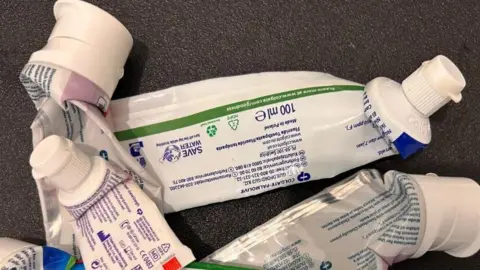 Picture of several empty toothpaste tubes. You can see the back of the toothpaste tubes with ingredients and various symbols including the recycling symbol. Many of the tubes are Colgate-branded toothpaste 