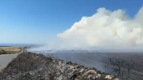 Fire at Lands End airport. A large plume of smoke coming from the end of the field which has been damaged by fire. 
