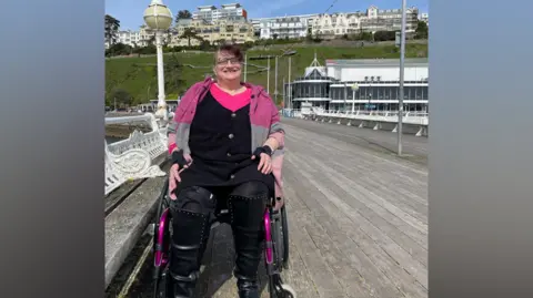 Dr Ali Carre Dr Ali Carre in a wheelchair smiles at the camera on a pier