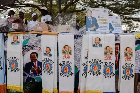 AFP People walk past stalls selling accessories bearing the image of Paul Biya, President of the Republic of Cameroon, to mark the 40th anniversary of Biya's rule in Yaounde on November 6, 2022. - Biya has served as president since November 6, 1982.