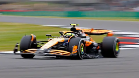 An orange McLaren Formula 1 car whizzes around the track at Silverstone.
