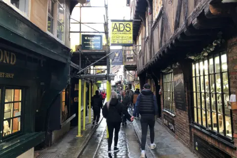 BBC / Naj Modak People walking along the Shambles street in York with Scaffolding which has gone up