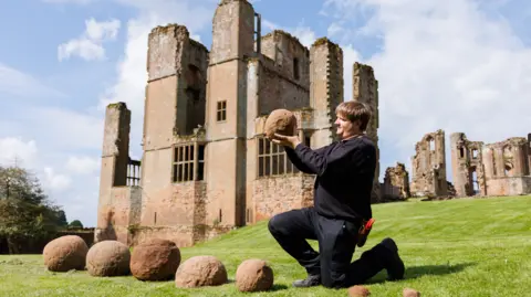 Kenilworth Castle The catapult shots lined up in front of the castle, with a man holding one of them