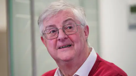 PA Media Mark Drakeford is an older man with glasses and white hair, wearing a red jumper.
