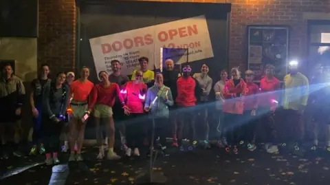 Night-time shot of several members of the run club. They're wearing multi-coloured running gear and standing in a line for the photo.